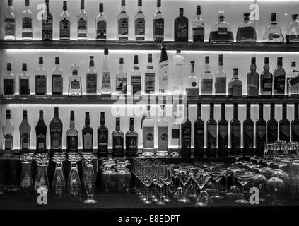 Les bouteilles de vin, des spiritueux ainsi que des lunettes sur un bar éclairé en arrière. Banque D'Images