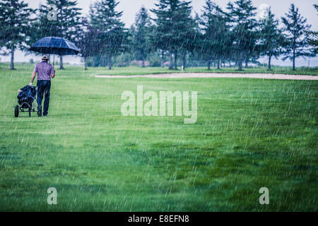 Golfeur sur un jour de pluie laissant le golf (le jeu est annulé à cause de la tempête) Banque D'Images