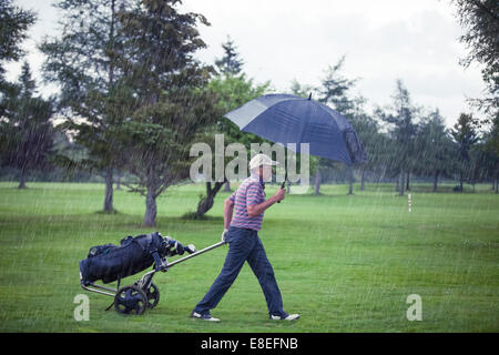 Golfeur sur un jour de pluie laissant le golf (le jeu est annulé à cause de la tempête) Banque D'Images