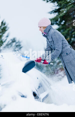 Femme enlever la neige à partir d'une voiture avec un balai après le Blizzard Banque D'Images