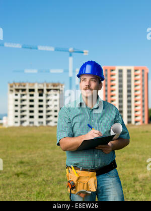 Ingénieur de race blanche debout, writing on clipboard, avec des bâtiments en construction sur l'arrière-plan Banque D'Images