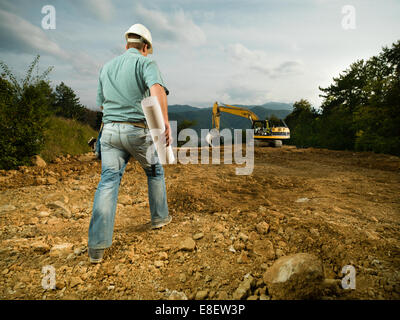 Vue arrière de l'engineer holding blueprint, randonnée pédestre sur le site de construction pelle vers Banque D'Images