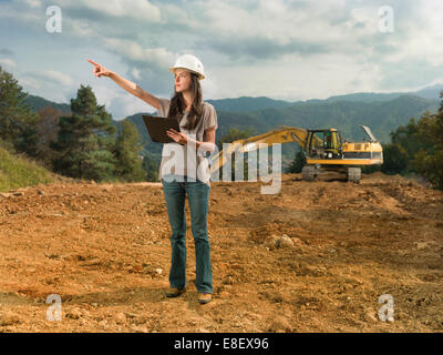 Portrait of young caucasian female architect at construction site, holding clipboard, pointant quelque chose Banque D'Images