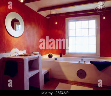 Miroir circulaire au-dessus du bassin en béton simple coiffeuse dans l'économie salle de bains avec murs effet éponge rouge Banque D'Images