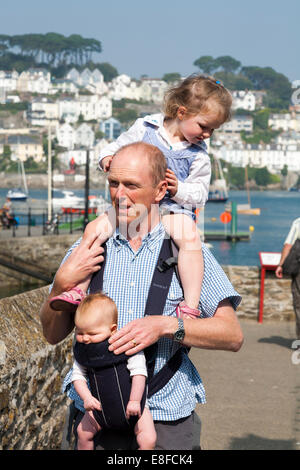 Papa mature / père avec 2 / 2 enfants ; un enfant sur les épaules et le bébé en écharpe. Cornwall UK. Banque D'Images