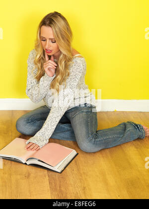 Ambiance détendue et informelle Positive confiante Jeune femme assise sur le sol de la lecture d'un livre ou d'étudier, sur un fond jaune vif, porter un jean bleu Banque D'Images