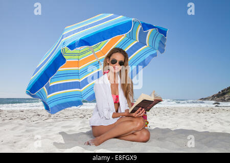 Femme lisant un livre sur la plage assis sous un parasol, le Cap, le Cap occidental, Afrique du Sud Banque D'Images