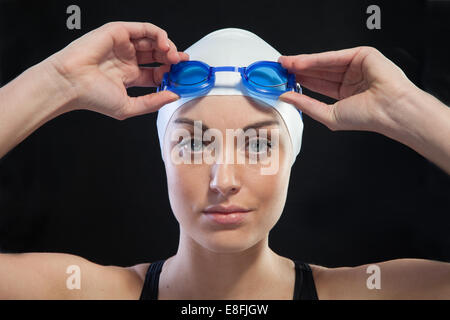 Portrait d'un nageur féminin avec lunettes bleues sur fond noir Banque D'Images
