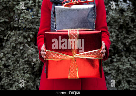 Gros plan d'une femme debout à l'extérieur devant un Bush tenant une pile de cadeaux de Noël Banque D'Images