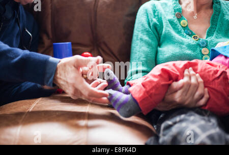 Petit-fils assis sur les genoux de grand-mère avec son grand-père chatouillant ses pieds Banque D'Images