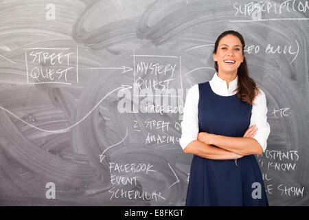 Portrait d'une femme debout devant un tableau noir avec ses bras croisés Banque D'Images