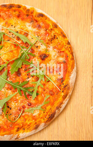 Gros plan d'une pizza au fromage et à la tomate avec une roquette sur une planche à découper en bois Banque D'Images