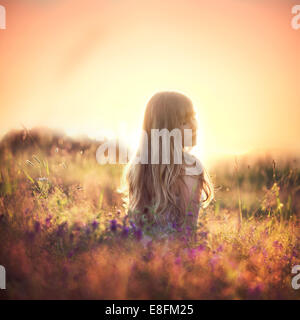 Femme assise dans un pré au coucher du soleil regardant sur son épaule, Norvège Banque D'Images