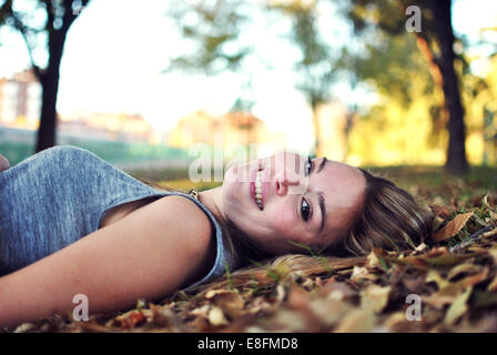 Portrait of smiling young woman lying on autumn leaves Banque D'Images