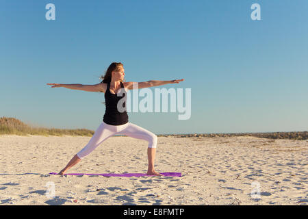 Woman practicing warrior 1 yoga pose sur plage Banque D'Images