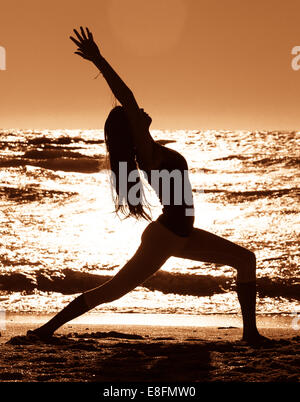 Silhouette of Woman practicing warrior 1 yoga pose sur plage Banque D'Images