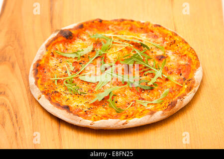 Pizza au fromage et aux tomates avec des flocons de piment et une roquette sur une table en bois Banque D'Images