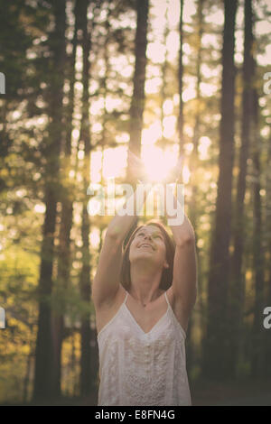 Portrait d'une femme debout dans une forêt prenant la lumière du soleil entre ses mains, Mississippi, États-Unis Banque D'Images