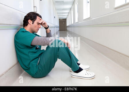 Médecin fatigué assis sur le sol dans un couloir d'hôpital Banque D'Images