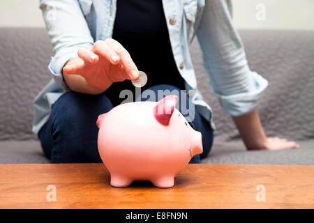 Woman putting coins en piggy bank Banque D'Images