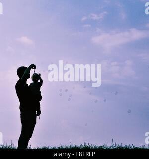 Silhouette d'homme et enfant blowing bubbles Banque D'Images