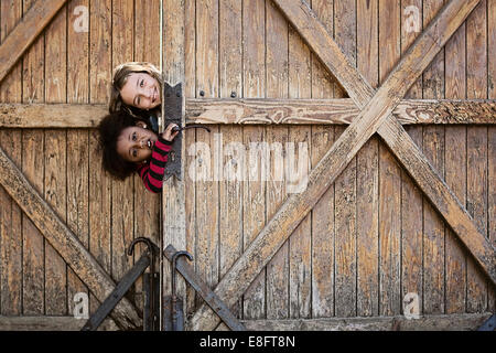 Deux filles peeking autour d'une porte en bois Banque D'Images