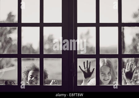 Deux jeunes filles à la recherche au travers d'une fenêtre Banque D'Images