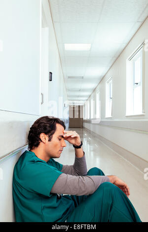 Médecin mâle fatigué assis dans le couloir de l'hôpital avec sa main sur son front Banque D'Images