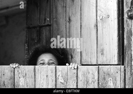 Girl peeking sur le bord d'une porte de l'écurie Banque D'Images