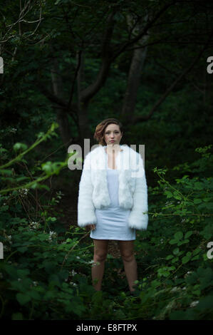 Un jeune androgyne aux yeux de biche à teenage femme fille portant une veste courte fourrure blanche, se trouvait seul à l'extérieur bois, soir UK Banque D'Images