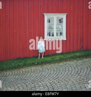 La Norvège, Girl (12-13) standing against red house