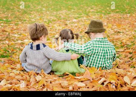Vue arrière de trois enfants assis dans les feuilles d'automne avec leurs bras autour l'un de l'autre, USA Banque D'Images