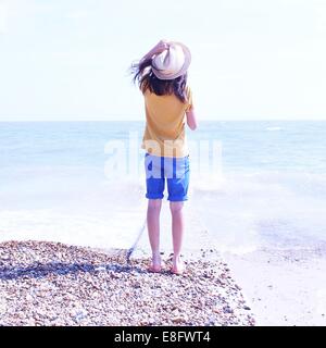 Vue arrière du Girl standing on beach holding hat