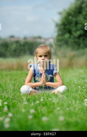 Girl (2-3) sitting on the grass doing yoga Banque D'Images