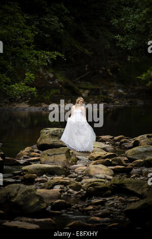 La robe "rebuts" : une jeune femme blonde girl wearing white ball modèle mariée robe de mariage robe debout dans la rivière à débit lent Banque D'Images