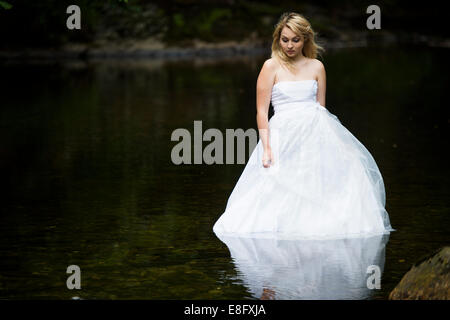 La robe "rebuts" : une jeune femme blonde girl wearing white ball modèle mariée robe de mariage robe debout dans la rivière à débit lent Banque D'Images