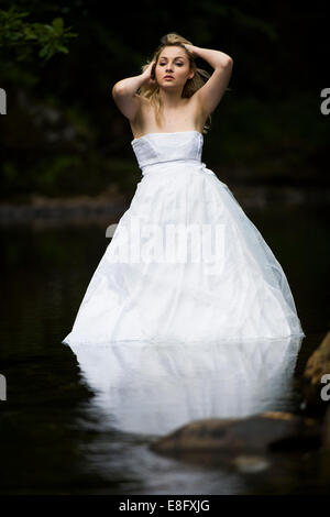 La robe "rebuts" : une jeune femme blonde girl wearing white ball modèle mariée robe de mariage robe debout dans la rivière à débit lent Banque D'Images