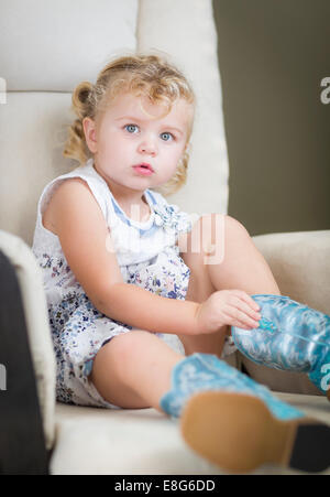 Blond aux yeux bleu adorable petite fille mettant sur bottes de cow-boy. Banque D'Images