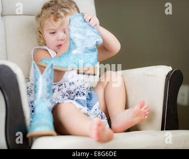 Blond aux yeux bleu adorable petite fille mettant sur bottes de cow-boy. Banque D'Images