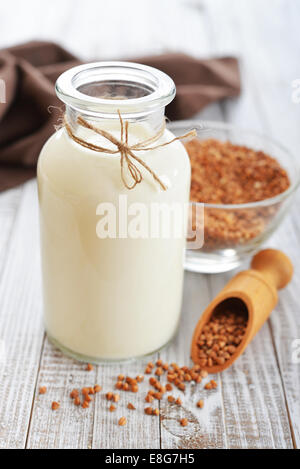 Le lait en bouteille avec sarrasin sarrasin graines sèches sur fond de bois blanc. Végétarien et Végétalien concept de lait. Banque D'Images