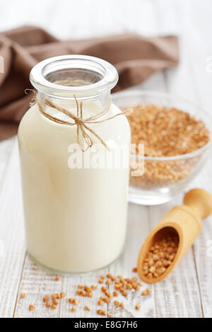 Le lait en bouteille avec sarrasin sarrasin graines sèches sur fond de bois blanc. Végétarien et Végétalien concept de lait. Banque D'Images