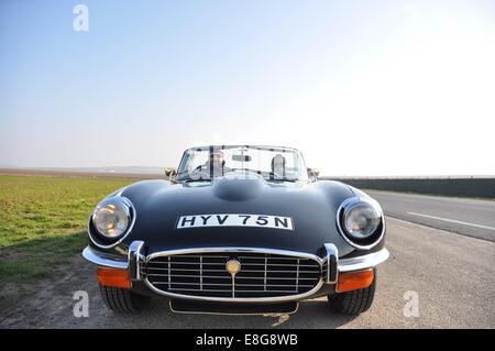 Un couple de 40 personnes, enveloppé contre le froid, conduisant une route Jaguar E-type V12, stationné à côté d'une route en France Banque D'Images