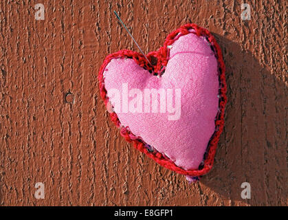 Décoration coeur fait main rose avec motif ornemental en dehors de pendre par aiguille sur fond de bois rouge Banque D'Images