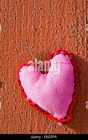 Décoration coeur fait main rose avec motif ornemental en dehors de pendre par aiguille sur fond de bois rouge Banque D'Images