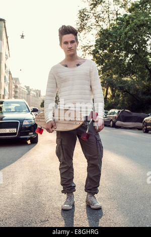 Portrait confiant homme high school student with skateboard article on city street Banque D'Images