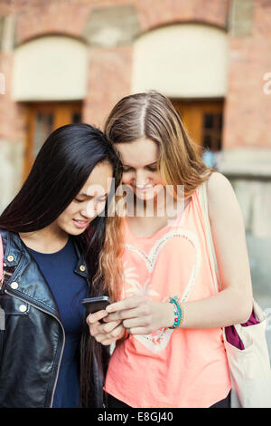 Femme amis Lire un message texte sur smart phone at high school de l'école Banque D'Images