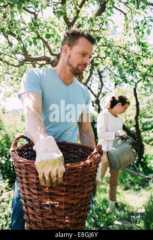 Homme portant panier en osier avec woman in background at yard Banque D'Images