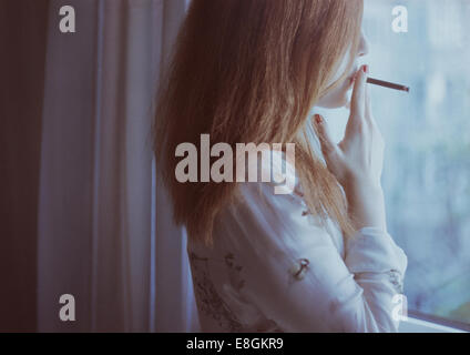 Portrait d'une femme debout par fenêtre fumeur Banque D'Images