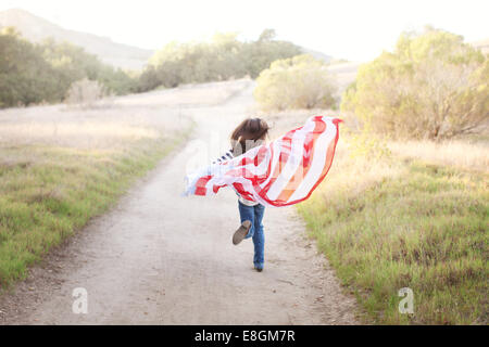 Vue arrière de Girl courir le long d'un sentier tenant un drapeau américain, USA Banque D'Images