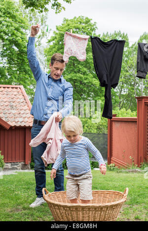 Girl standing in panier de blanchisserie pendant que le père dépose de vêtements de corde Banque D'Images